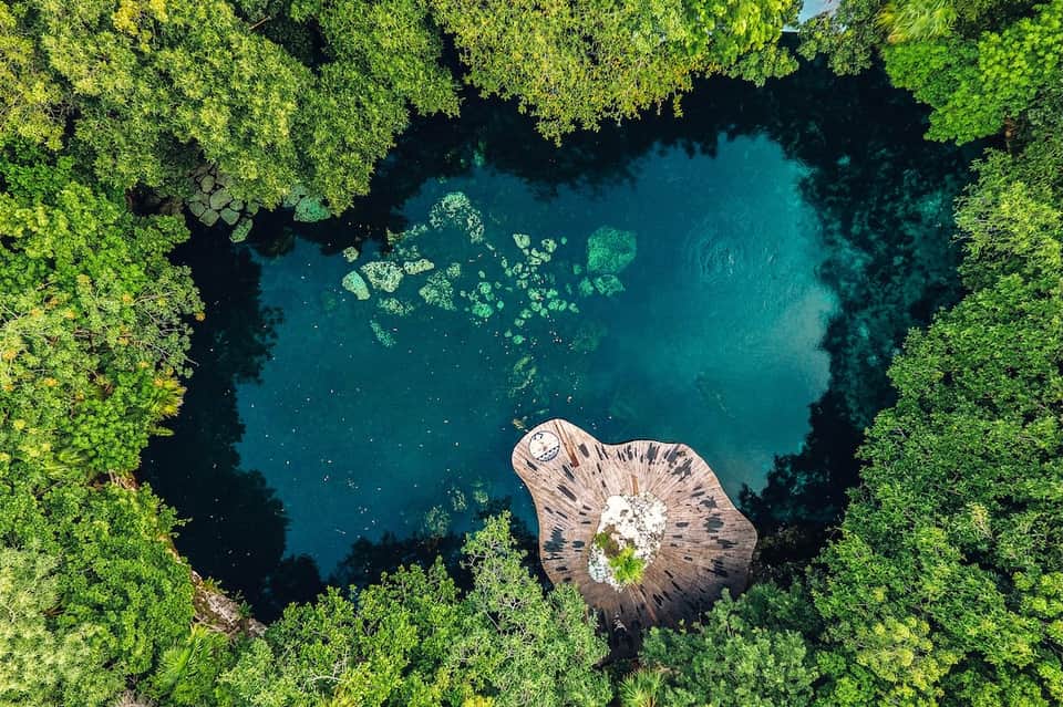 Aerial view of cenote with crystal blue water surrounded by dense green jungle and rocky formations