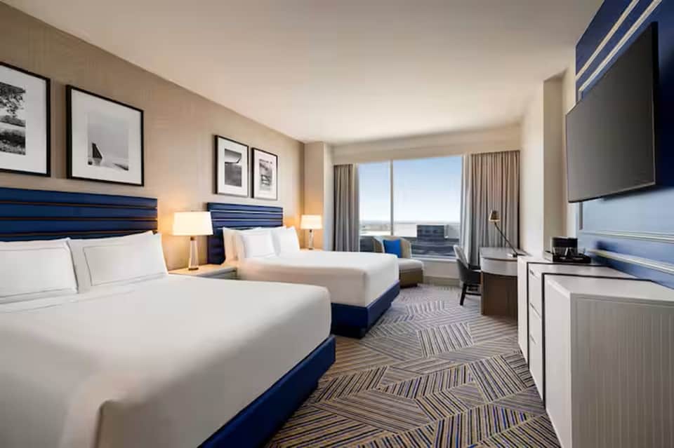 Modern hotel room with two queen beds, blue headboards, and panoramic window views