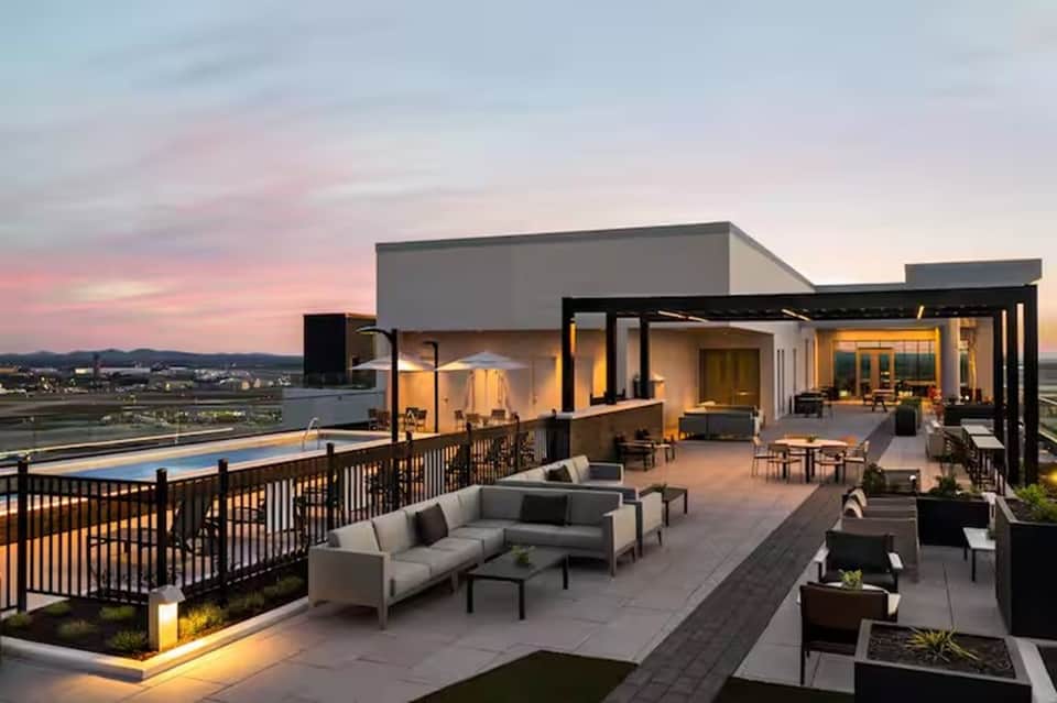 Modern rooftop terrace at sunset with pool, lounge seating, and city skyline views