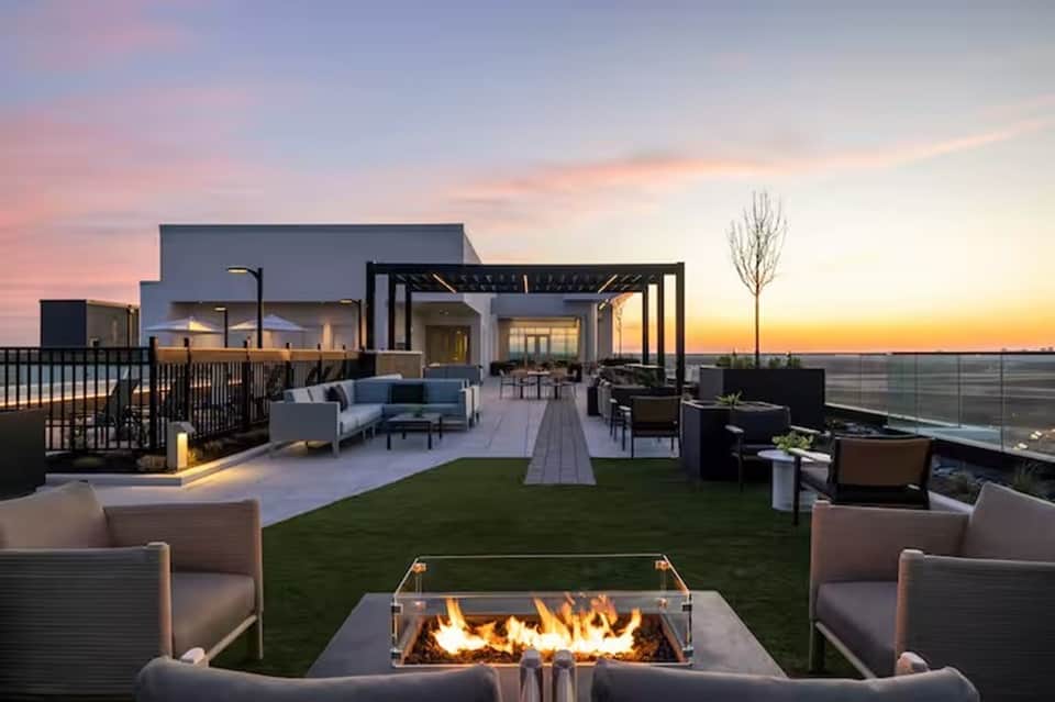 Rooftop terrace at sunset with fire pit, lounge seating, artificial grass, pergola, and panoramic water views
