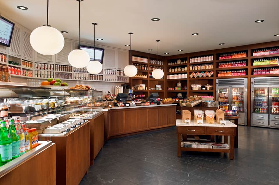 Upscale café interior with wooden cabinetry, glass display cases, pendant lighting, and refrigerated units