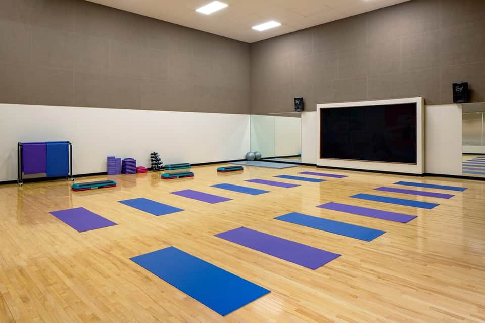 Yoga and fitness studio with wooden floor, purple and blue mats, and large display screen