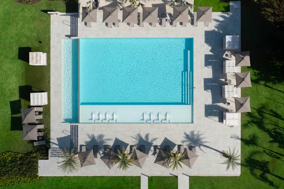 Aerial view of rectangular pool with surrounding lounge chairs and dark umbrellas on concrete patio