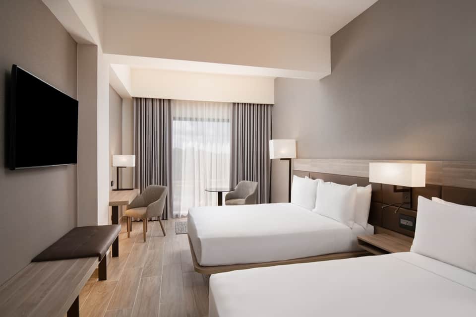 Contemporary hotel room with two queen beds, modern furnishings, flat-screen TV, and floor-to-ceiling windows