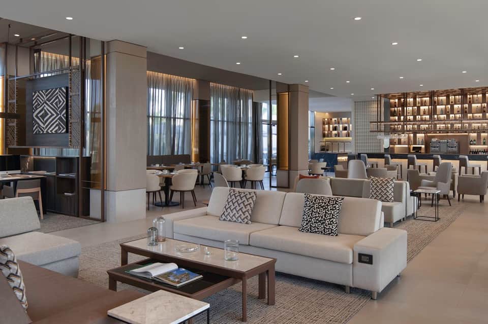 Contemporary hotel lounge with neutral furniture, bar area, and ambient lighting