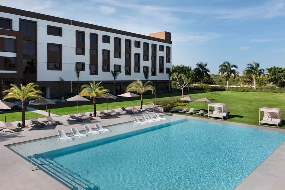 Contemporary resort pool with white loungers, manicured lawn, and modern white building