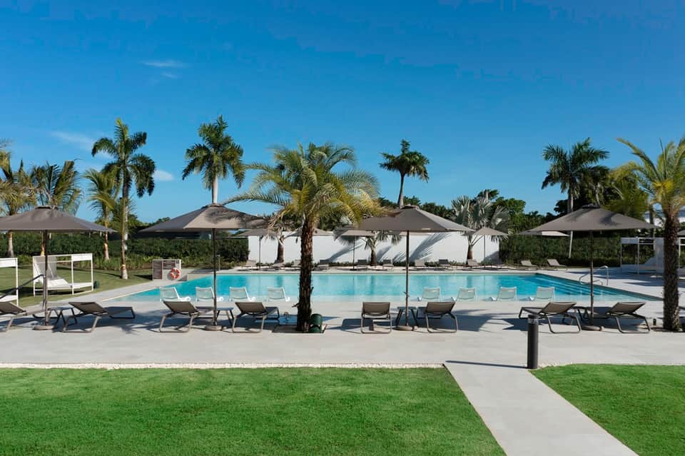 Resort pool with lounge chairs, black umbrellas, white cabanas, and tropical palm tree landscaping
