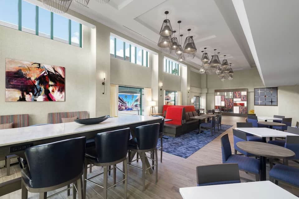 Modern hotel lobby with high ceilings, pendant lights, dining area, and lounge seating