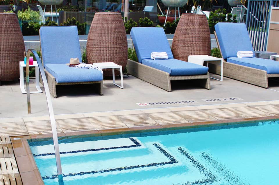 Resort pool deck with blue lounge chairs, wicker privacy screens, and clear turquoise swimming pool