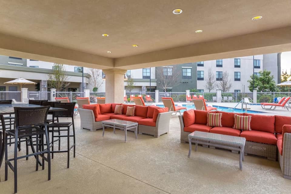 Covered patio lounge with red and orange seating, bar area, and resort pool in background