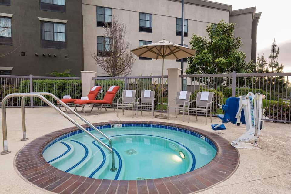 Spa hot tub surrounded by lounge chairs and umbrellas with resort building backdrop