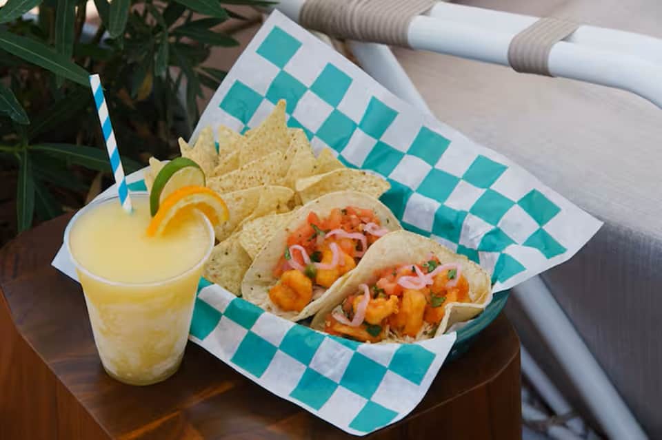Poolside tacos and lemonade served on turquoise and white checkered paper with tropical poolside setting