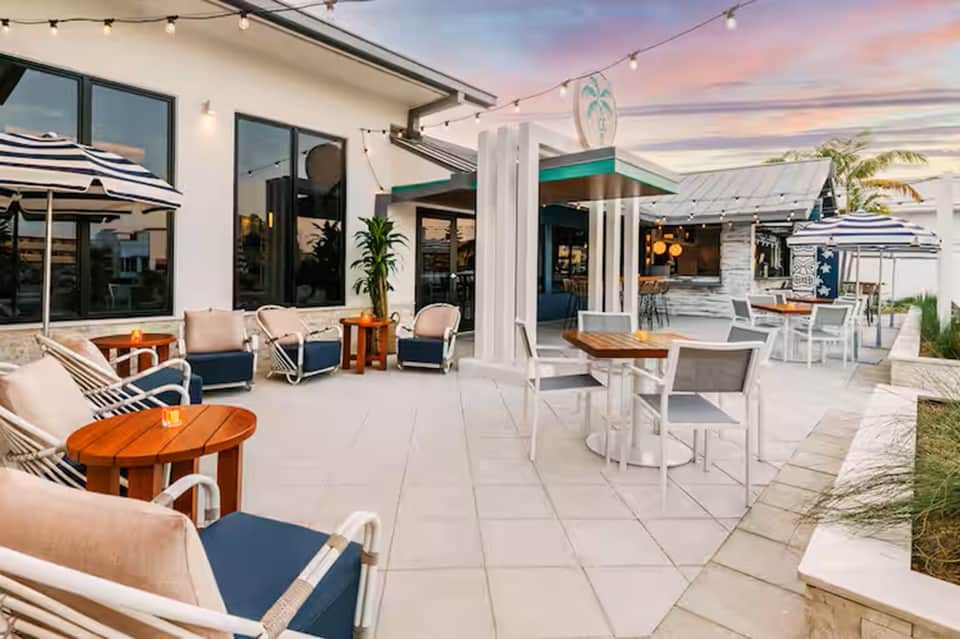 Modern outdoor patio with lounge seating, dining tables, string lights, and sunset views