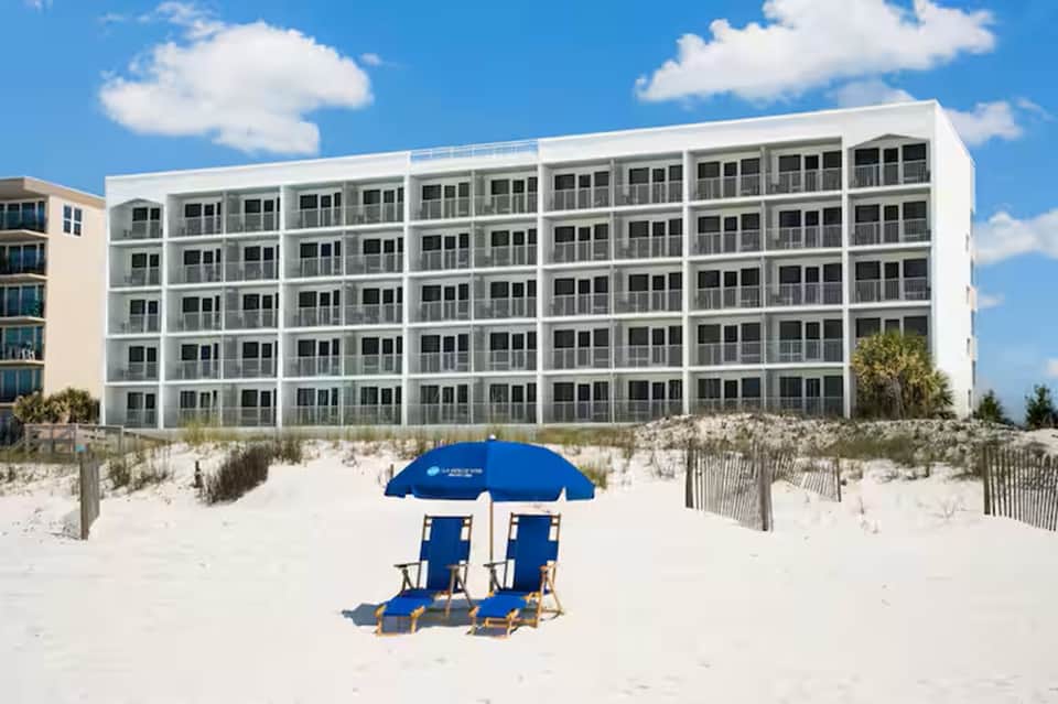 White beachfront condominium building with blue umbrellas on sandy beach