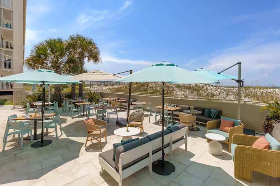 Beachfront terrace with turquoise umbrellas, lounge chairs, and ocean view with palm trees