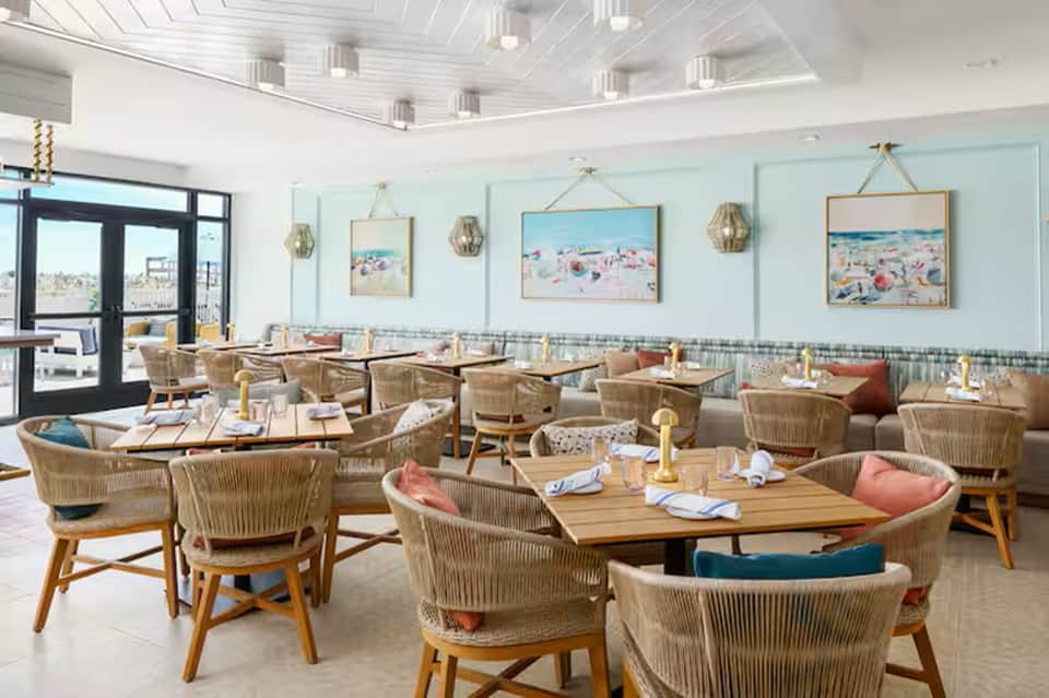 Casual resort dining room with light blue walls, woven chairs, and beach-themed artwork