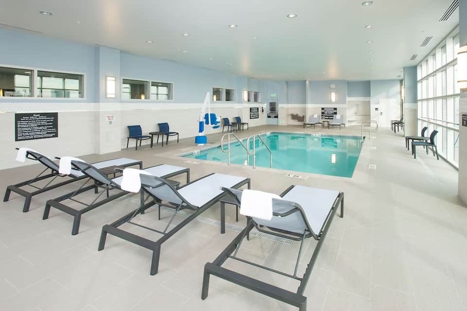 Indoor heated pool facility with lounge chairs, blue water, large windows, and modern amenities