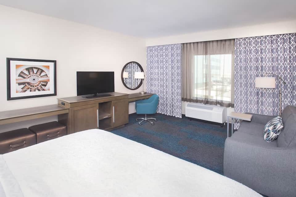 Contemporary hotel suite with white bed, desk with TV, patterned curtains, and seating area