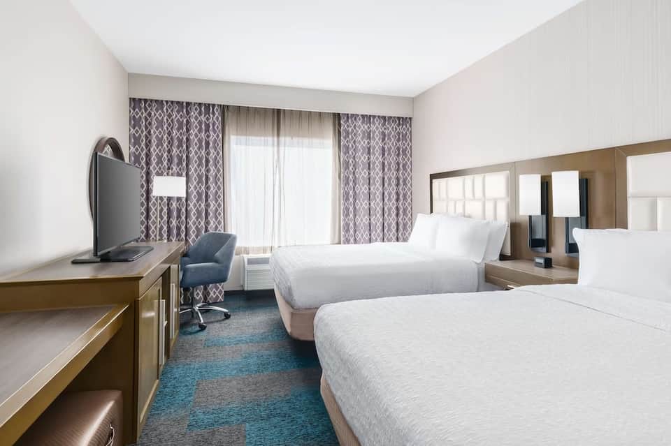 Hotel double queen bedroom with patterned curtains, flat-screen TV, and bathroom vanity