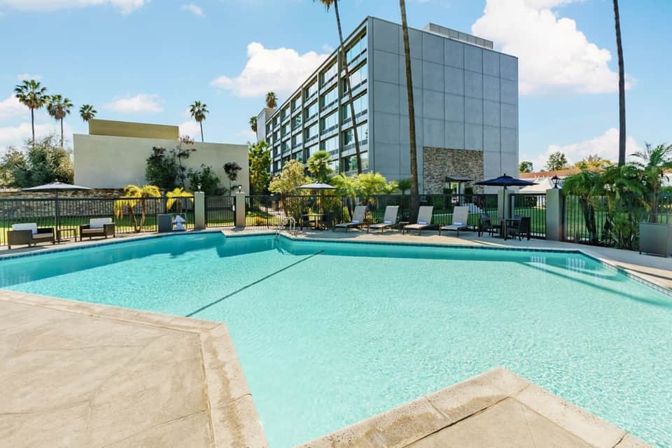 Resort swimming pool with turquoise water, lounge chairs, palm trees, and modern hotel building