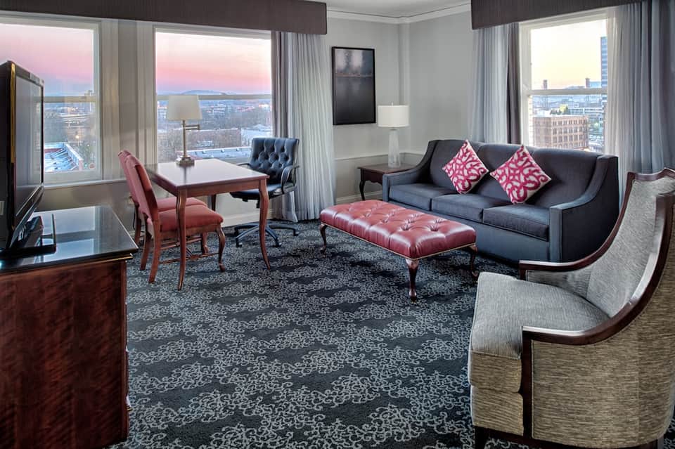 Luxury suite with city views, gray sofa with pink pillows, and floor-to-ceiling windows