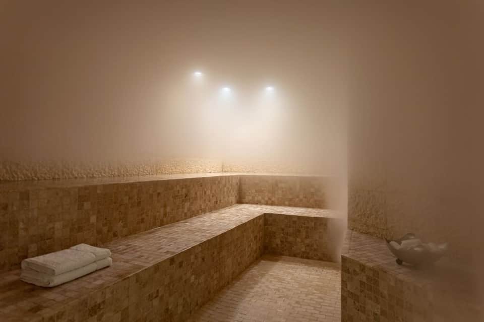 Serene spa steam room with cream-colored tile walls, bench seating, and soft overhead lighting