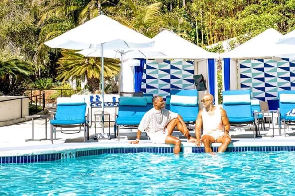 Couple relaxing in resort pool with blue loungers and white umbrellas under palm trees