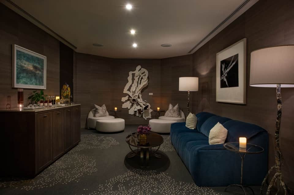 Luxury spa lounge with dark wood walls, blue curved sofa, and artistic sculptures