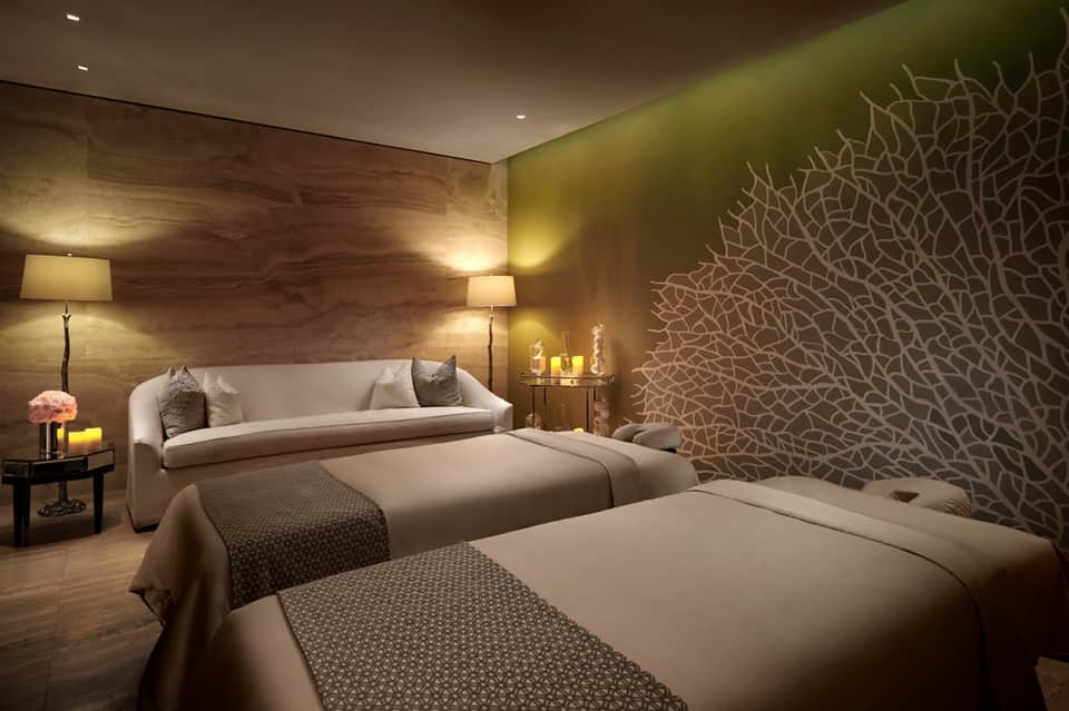 Luxurious spa bedroom with two beds, decorative wall art, wood accents, sofa, and ambient lighting