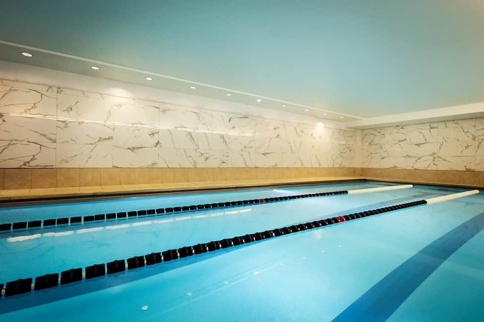 Indoor lap pool with lane dividers, marble walls, and soft lighting for swimming laps