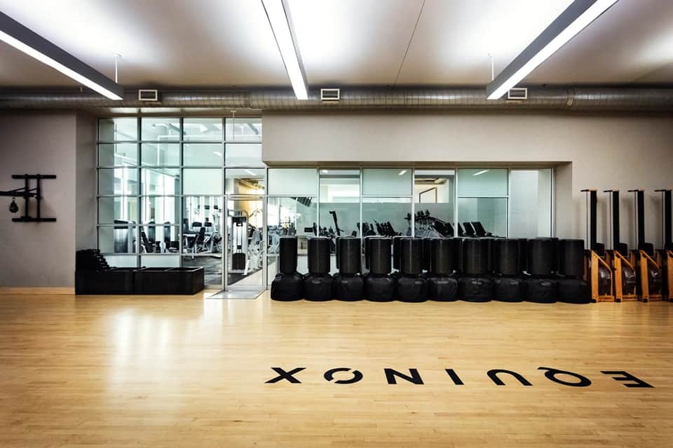 Modern fitness studio with wooden floors, black exercise equipment, and glass-walled gym visible