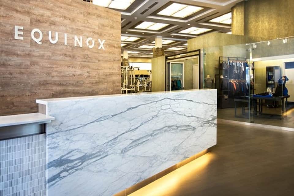 Upscale hotel lobby with marble reception desk, wooden accent wall, and EQUINOX signage