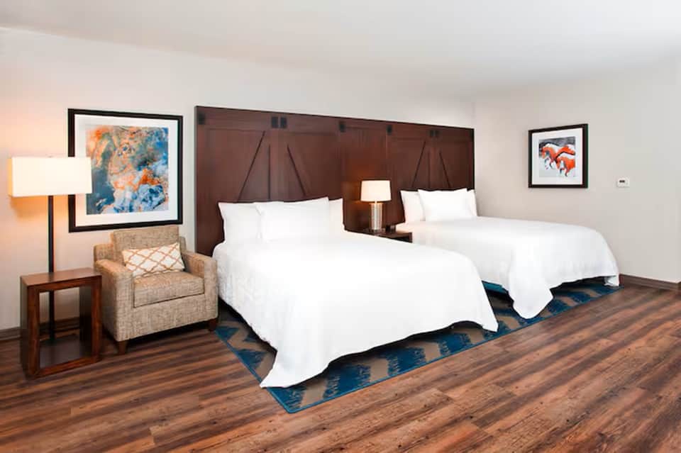Hotel room with two queen beds, wooden headboard, artwork, and warm neutral decor