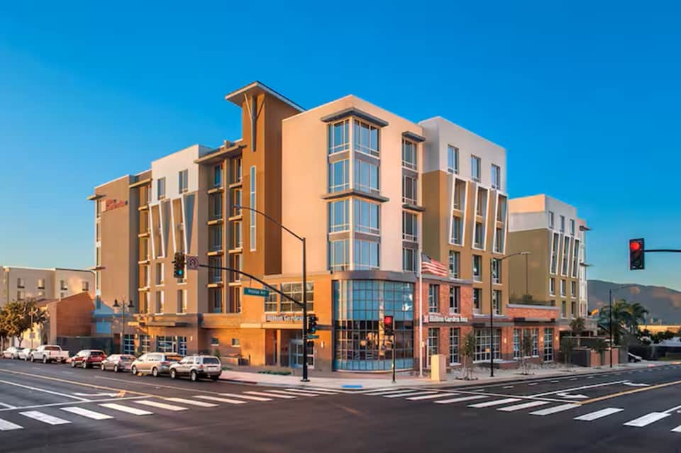 Contemporary mixed-use building with warm orange and beige facade, multiple stories, street-level retail, clear blue sky