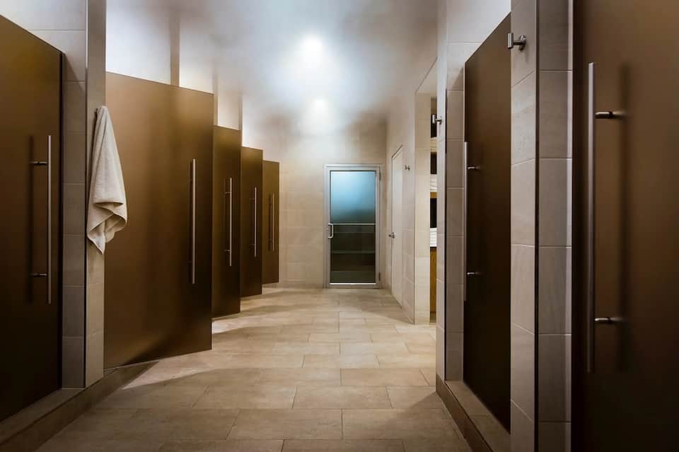 Hotel locker room hallway with individual lockers, mirrors, and neutral tile flooring