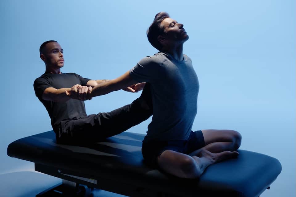 Two people performing assisted stretching exercise outdoors against blue sky in wellness therapy session
