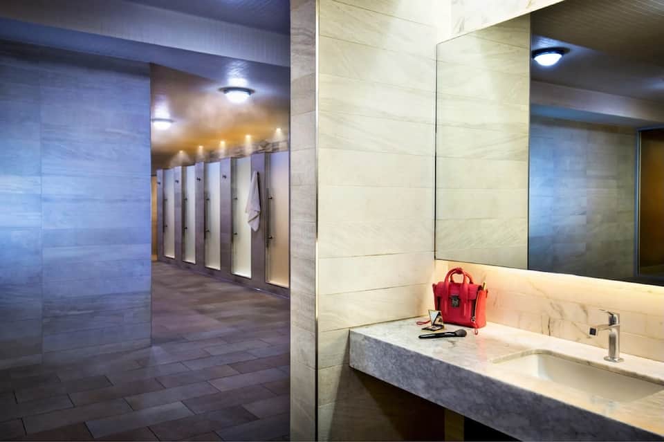 Modern spa locker room with beige tile walls, private changing areas, and illuminated vanity mirror
