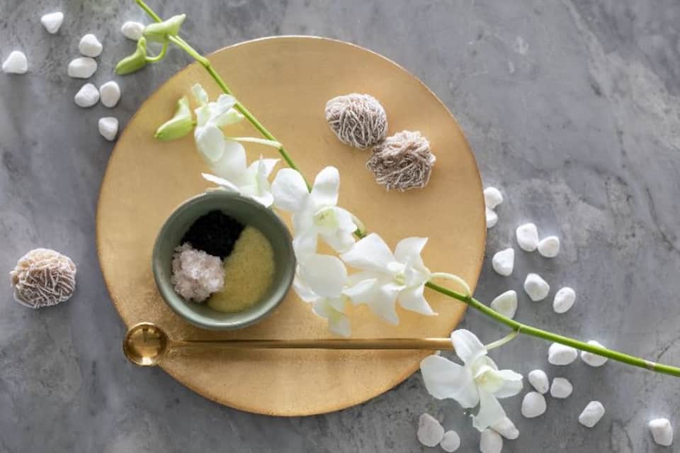 Spa styling flat lay with gold dish, white orchid flowers, sea salt, and natural spa accessories
