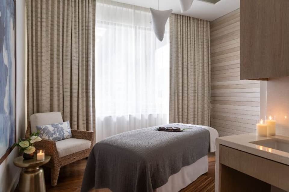 Spa treatment room with massage table, natural light, wooden accents, and candles