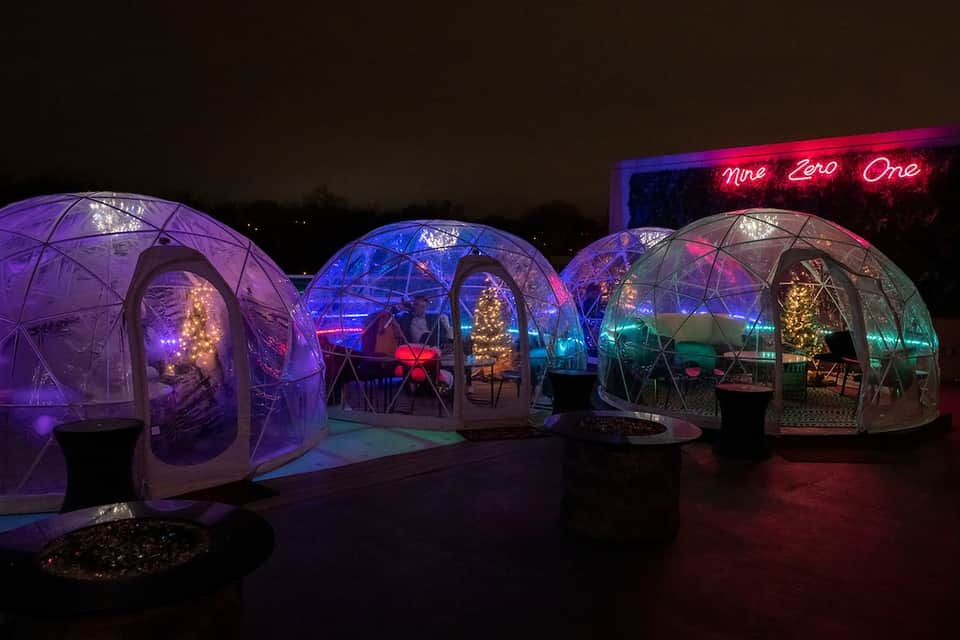 Illuminated dining igloo pods with colorful LED lighting and neon signs at night
