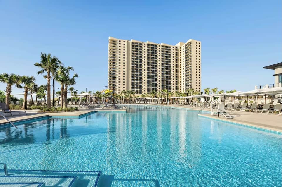 Resort-style pool with cream high-rise building, palm trees, and lounge chairs