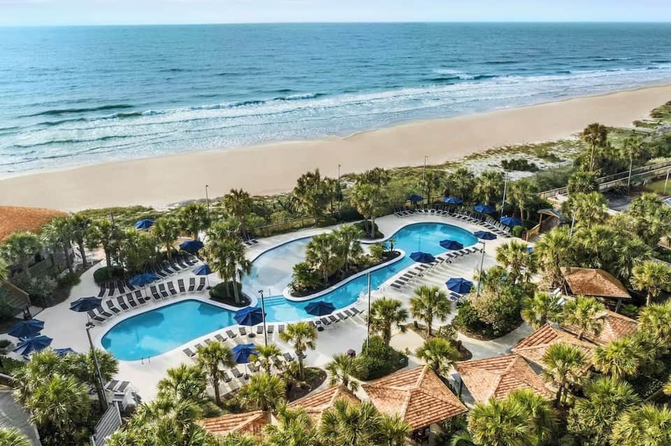 Curved swimming pools with palm trees, lounge chairs, and ocean beach view