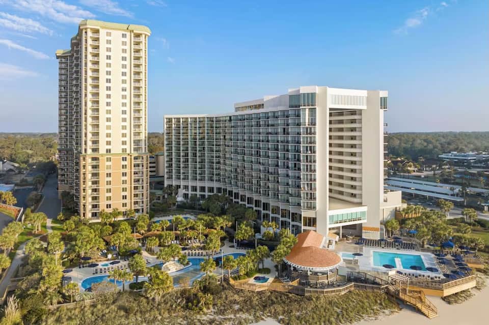 Beachfront resort towers with multiple pools, palm trees, and ocean views during daytime