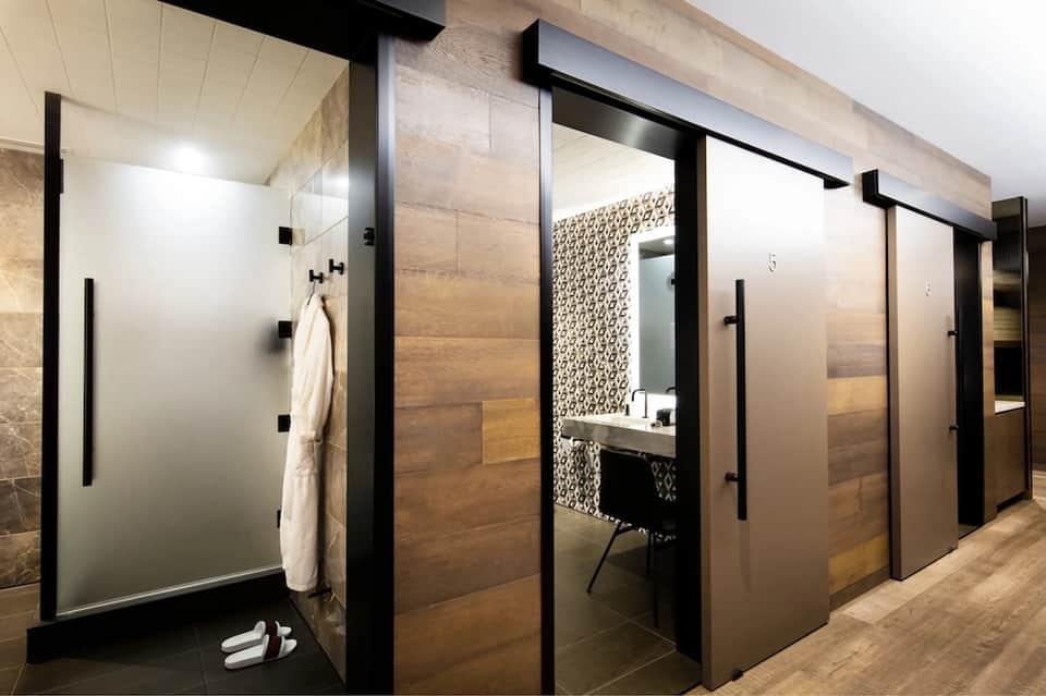 Contemporary spa changing room corridor with wooden doors, glass shower enclosure, stone walls, and neutral tones