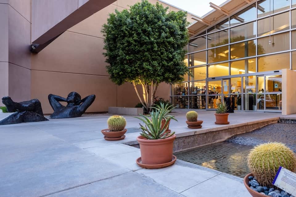 Modern courtyard with art sculpture, potted plants, and glass-fronted building entrance