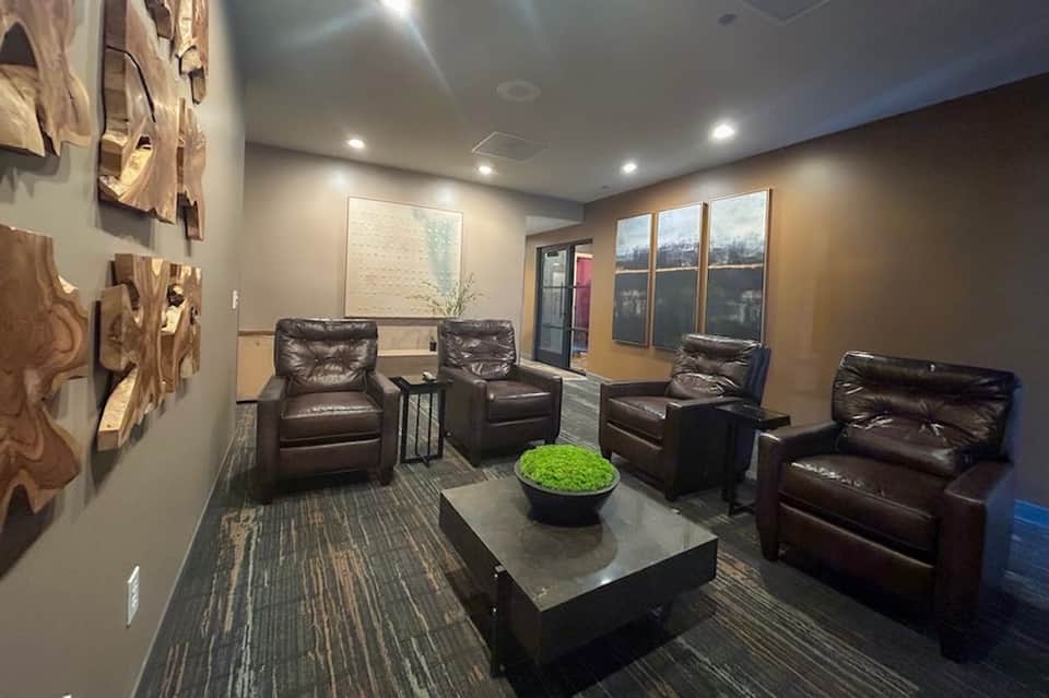 Modern lounge with leather recliners, decorative wall art, large windows with city views, and contemporary decor