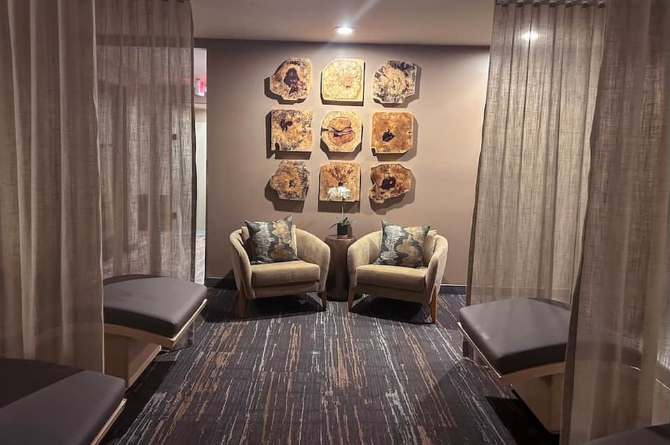 Spa relaxation lounge with cream armchairs, decorative wall art, and sheer curtains