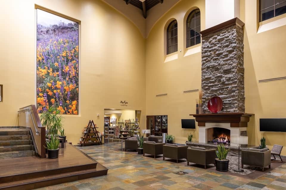 Grand resort lobby with high ceilings, fireplace, stone accents, yellow walls, large floral artwork, and elegant furnishings