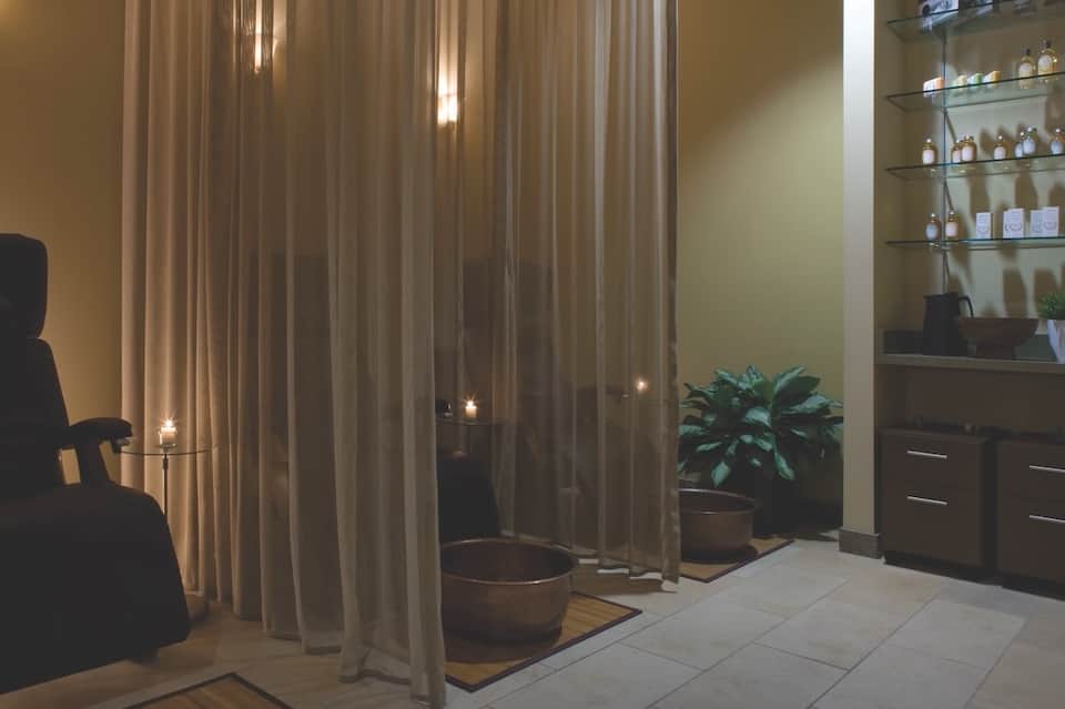 Spa treatment room with sheer curtains, shelving with products, and modern amenities lighting