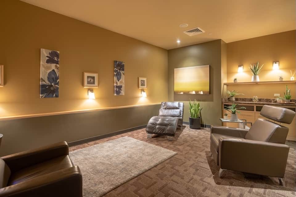 Luxurious spa relaxation room with tan and brown tones, comfortable seating, and ambient lighting
